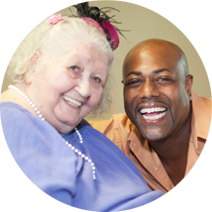 Smiling man and woman, she is wearing a lavender shirt and festive pink hat
