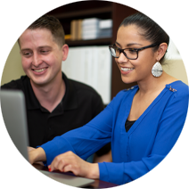 Professional woman in a bright blue top and black frame glasses typing on a computer