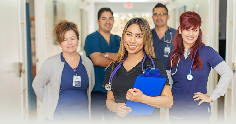 3 female healthcare workers smiling in front with two male healthcare works in the back
