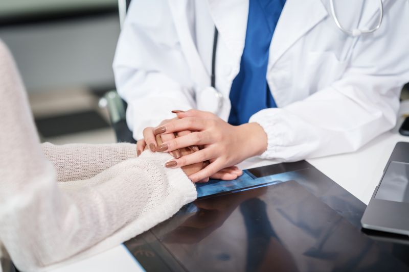 View of the hands of a nurse comforting a family member by holding hands
