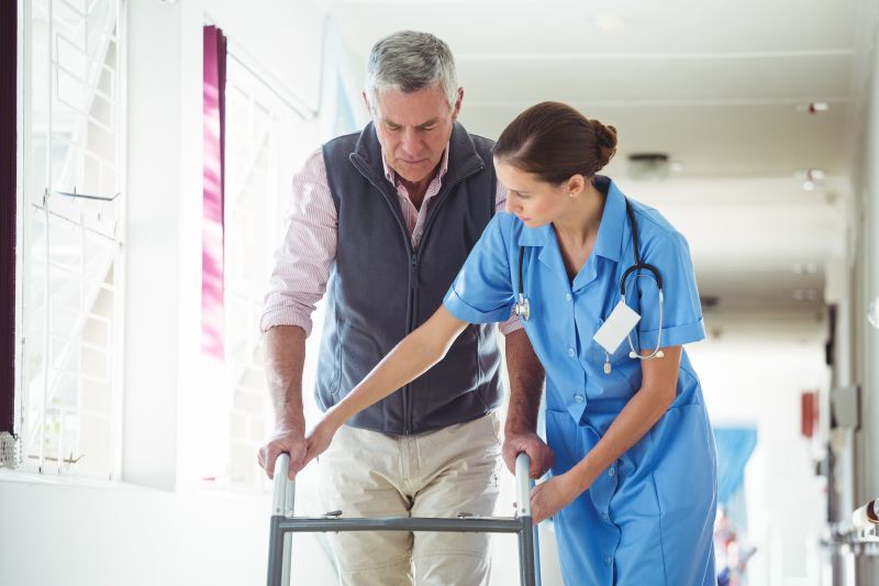 Nurse helping patient use a walker in a hallway