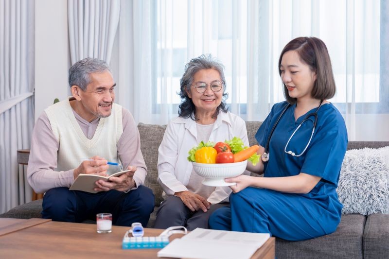 Nurse holding a bowl of vegetables discussing nutrition with an older couple
