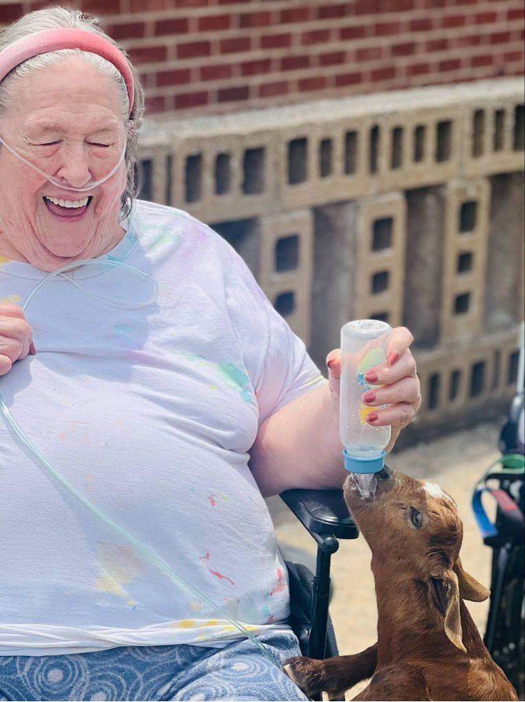 patient-goat2 Linley Park resident smiling while feeding a bottle to a baby goat
