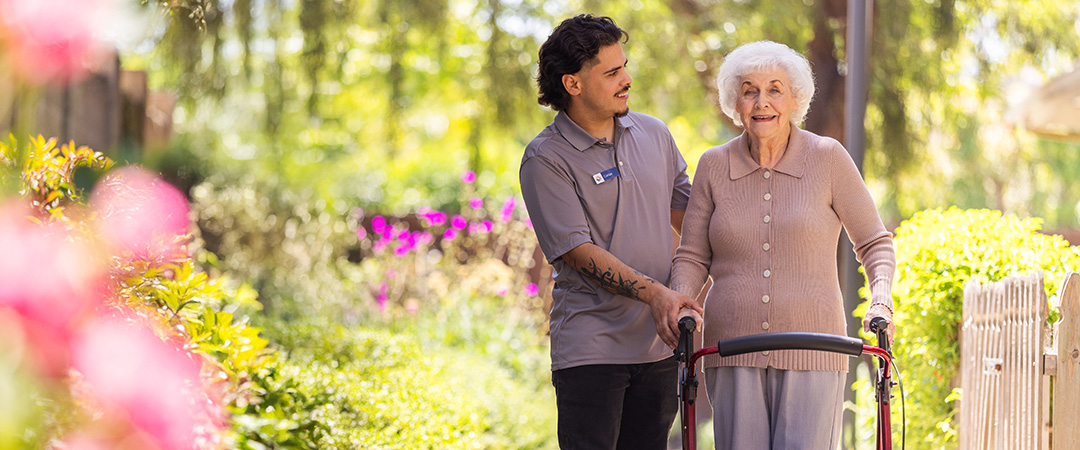 An elderly woman walking with a caretaker
