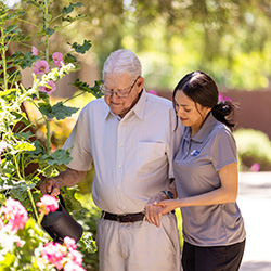 An elderly man walking outside with a caretaker
